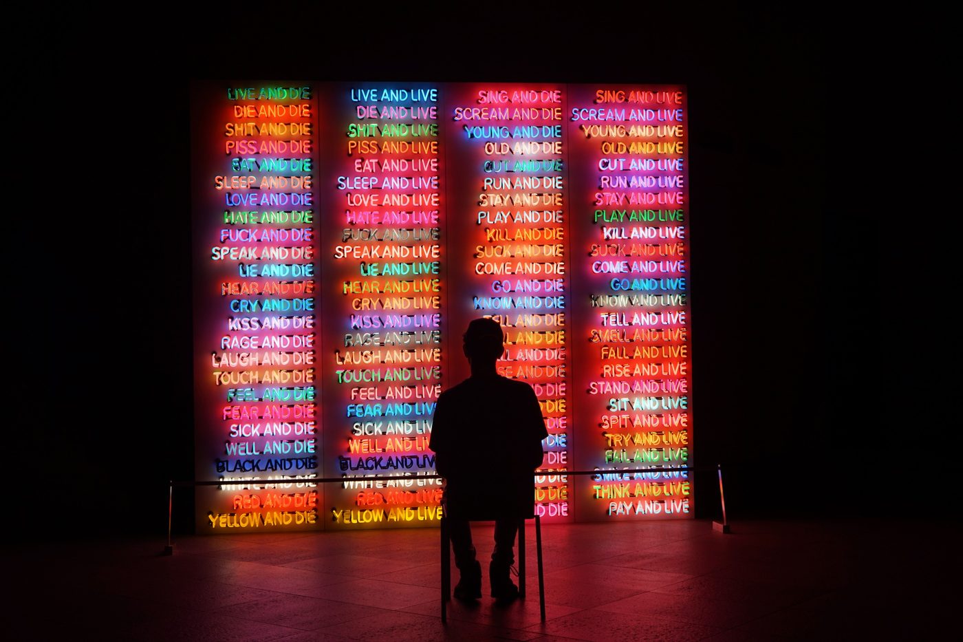 A visitor seated before a wall of multicoloured neon phrases