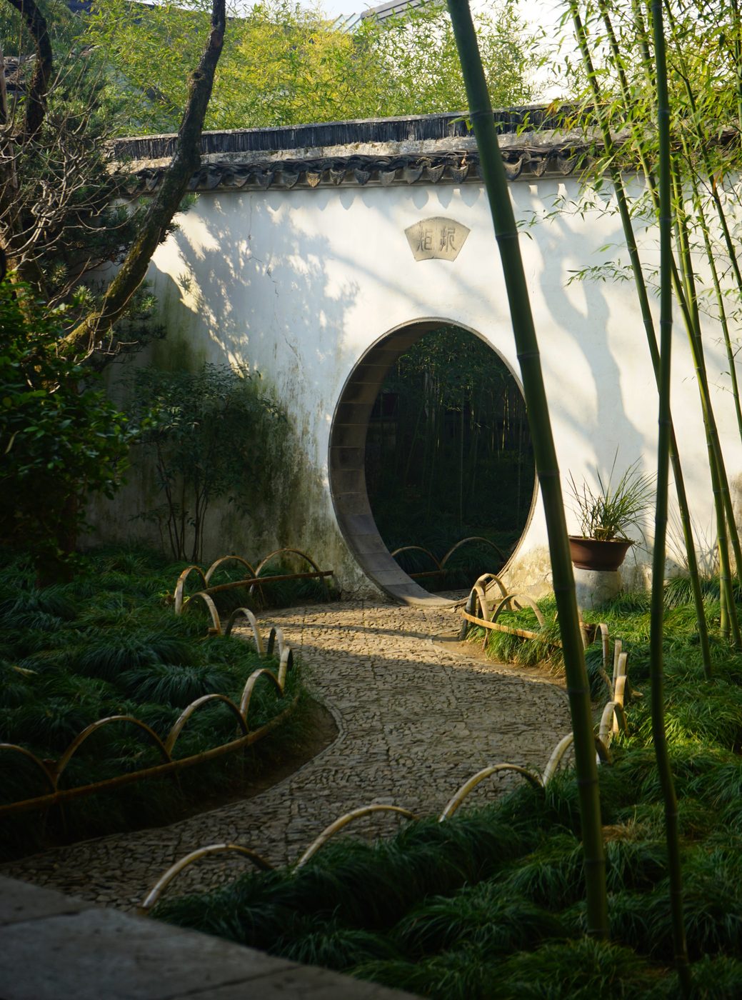 A round moon gate in a white garden wall, framed by bamboo and a winding stone path